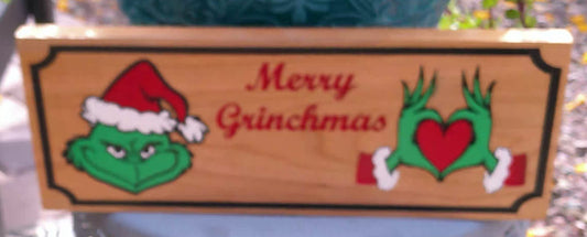 Wooden sign with Grinch face and text 'Merry Grinchmas' on a blurred background