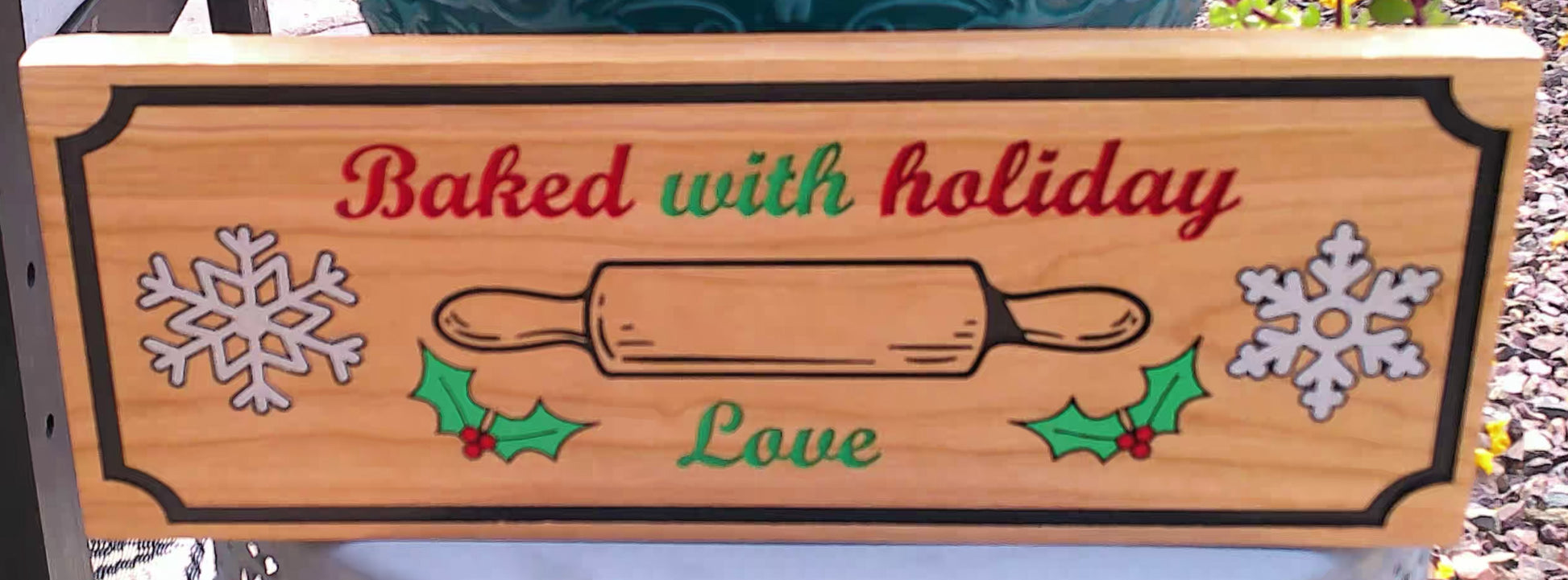 Wooden sign with holiday-themed design and text 'Baked with holiday love' on a blurred outdoor background.