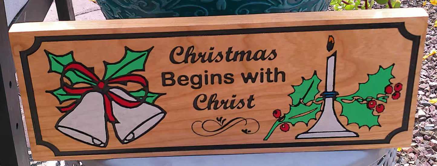 Wooden sign with Christmas design featuring bells and a candle, with text 'Christmas Begins with Christ'.