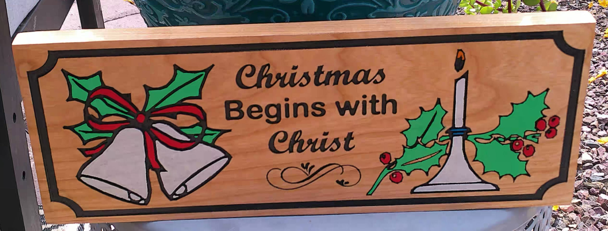 Wooden sign with Christmas design featuring bells and a candle, with text 'Christmas Begins with Christ'.