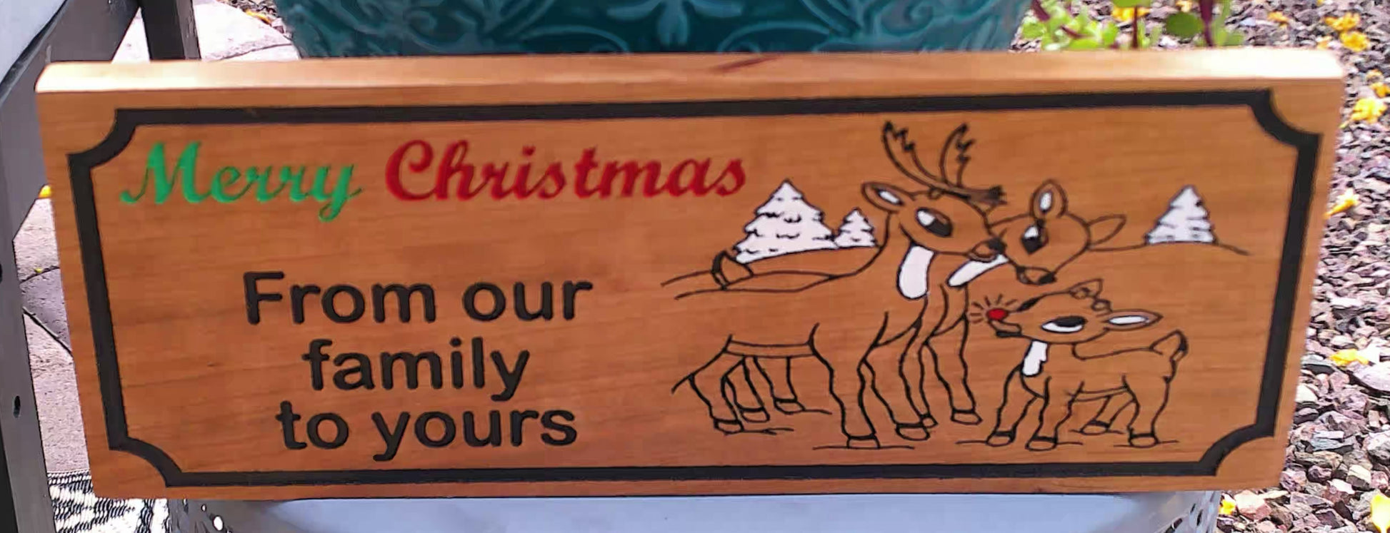 Wooden Christmas sign with reindeer illustration and text 'Merry Christmas from our family to yours'.