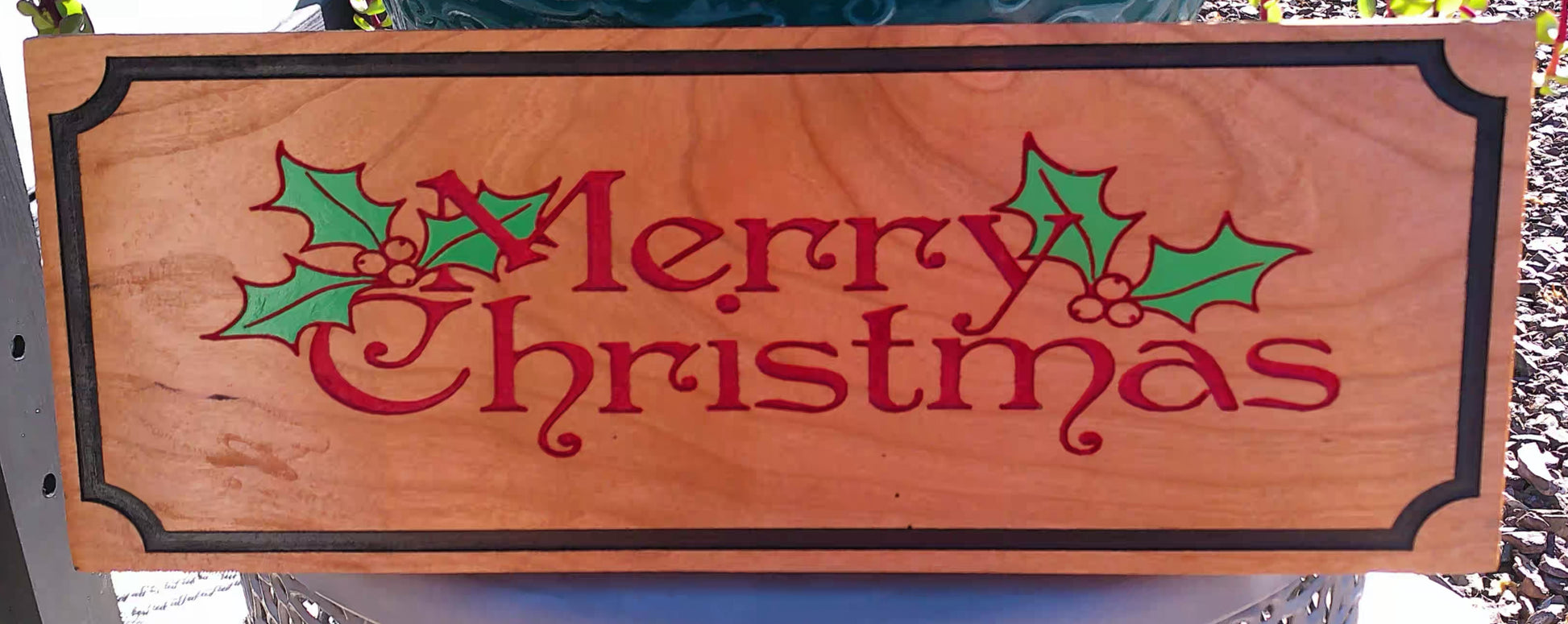 Wooden sign with 'Merry Christmas' text and holly leaves on a natural background