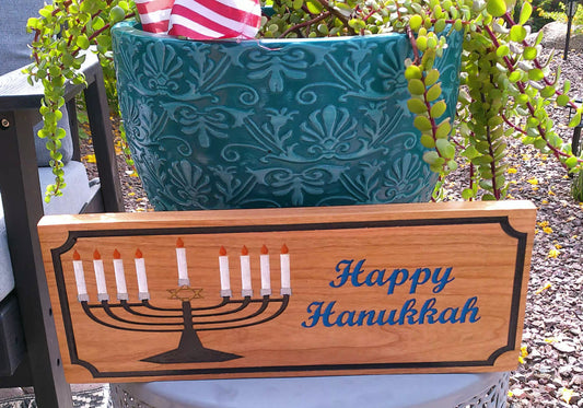 Wooden sign with Menorah design and 'Happy Hanukkah' text, placed outdoors.