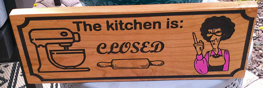 Wooden sign with a cartoon character and text 'The kitchen is: CLOSED' on a wooden surface.