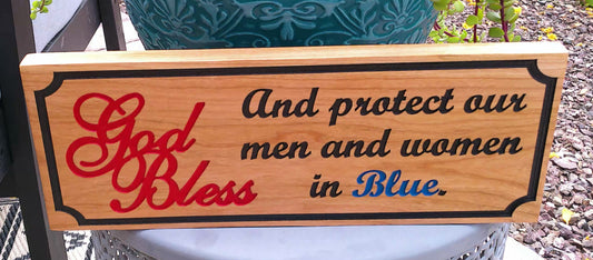 Wooden sign with engraved text 'God Bless and protect our men and women in Blue' on a blurred background.