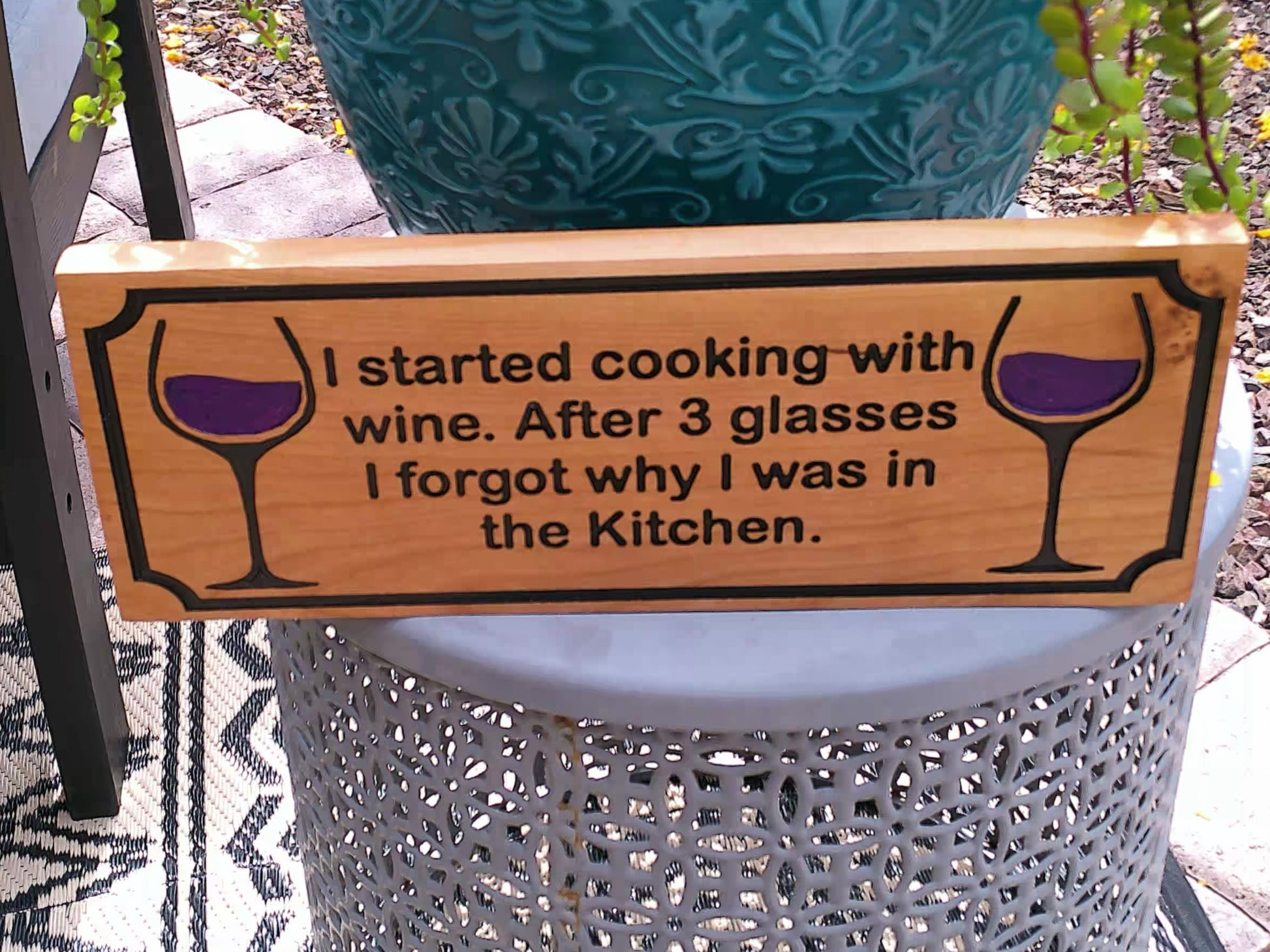 Wooden sign with wine-themed text and graphics on a stand outdoors.
